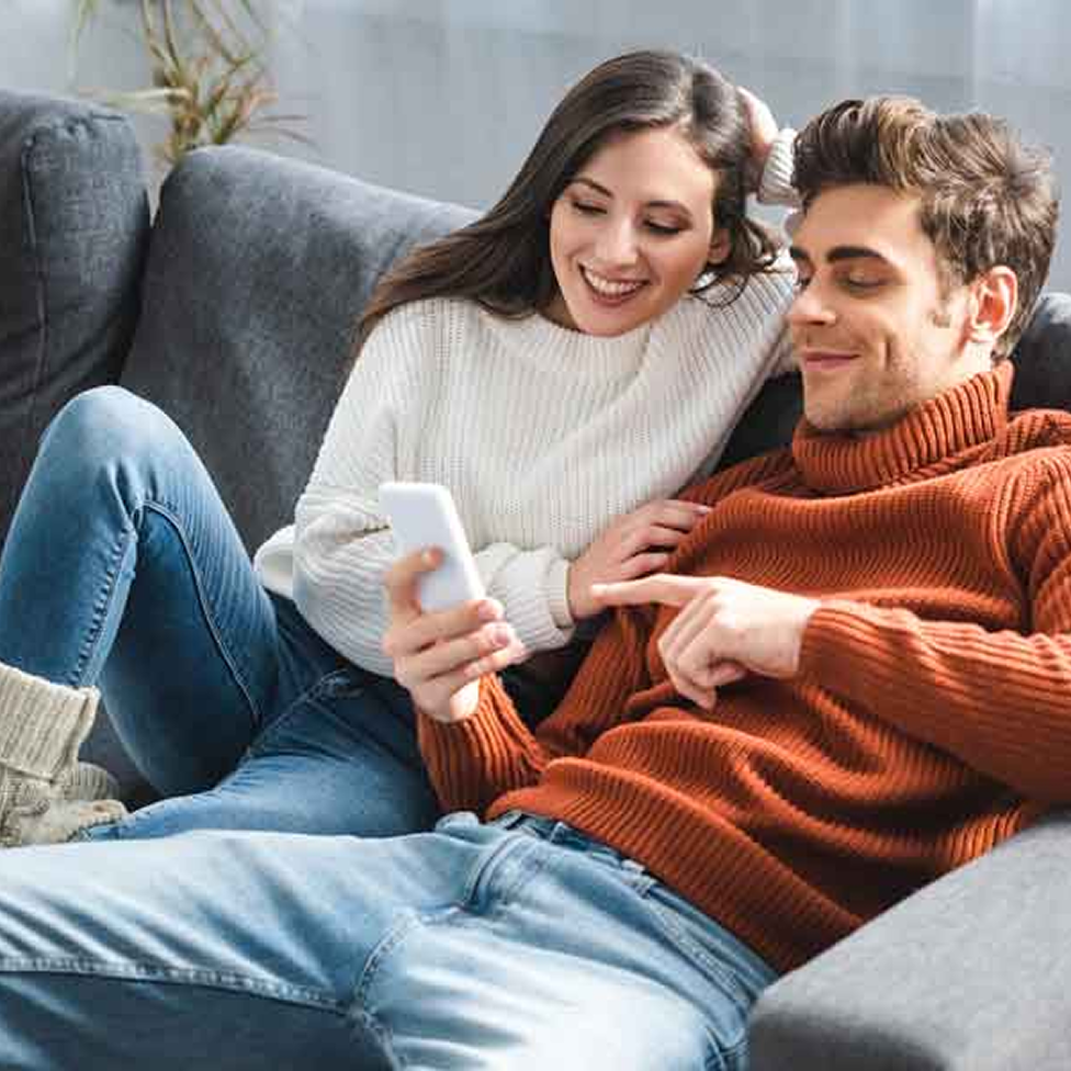 A couple on a couch looking at a phone in one of their hands.