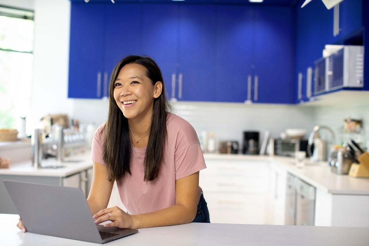 Woman smiling using her laptop in kitchen